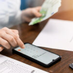 Person calculating expenses on a smartphone while holding cash, illustrating how to transfer money from Oman securely and efficiently