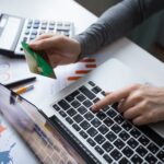 Person making an online money transfer using a laptop and debit card, representing the best money transfer to Pakistan from Oman..